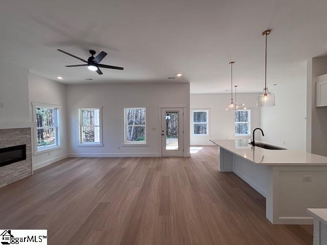 550 Vault Way, Roebuck, SC 29376 - unfurnished living room with a stone fireplace, a sink, ceiling fan with notable chandelier, and light wood-style floors