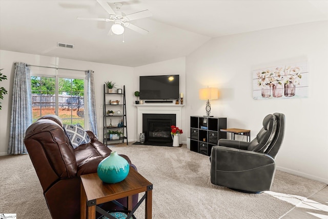carpeted living area featuring visible vents, lofted ceiling, baseboards, ceiling fan, and a fireplace with flush hearth