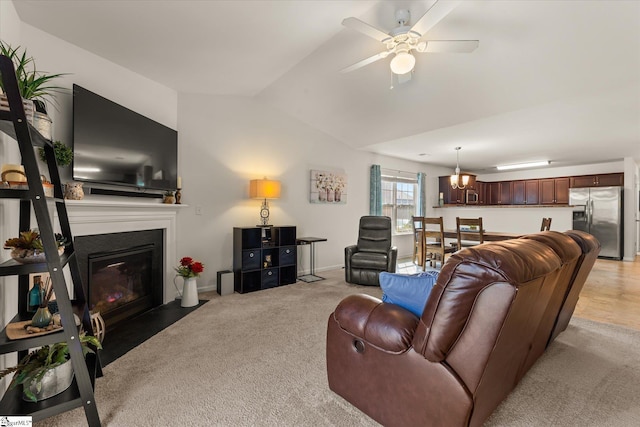 living area with light colored carpet, a fireplace with flush hearth, a ceiling fan, and vaulted ceiling