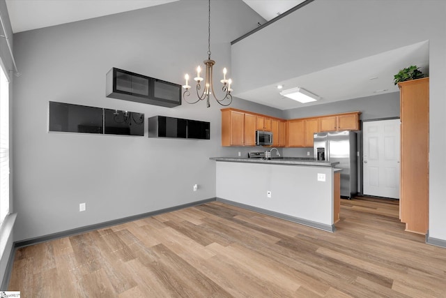 kitchen featuring appliances with stainless steel finishes, a peninsula, light wood-style flooring, and a notable chandelier