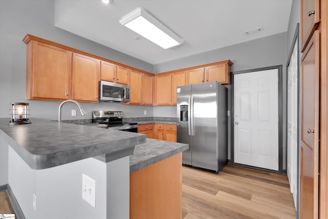 kitchen with dark countertops, light wood finished floors, stainless steel appliances, a peninsula, and visible vents