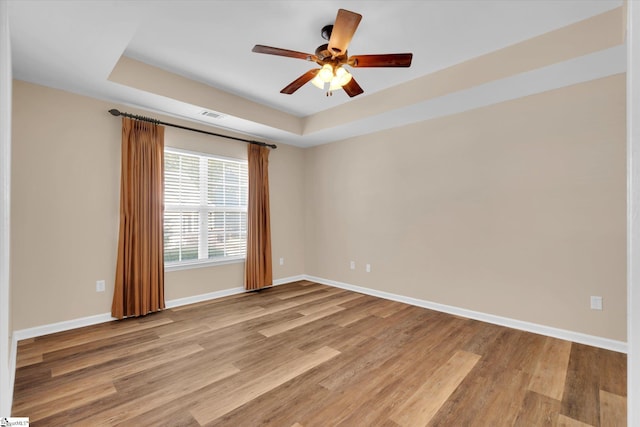 unfurnished room with visible vents, baseboards, ceiling fan, a raised ceiling, and light wood finished floors