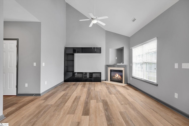 unfurnished living room featuring a glass covered fireplace, high vaulted ceiling, a ceiling fan, and light wood finished floors