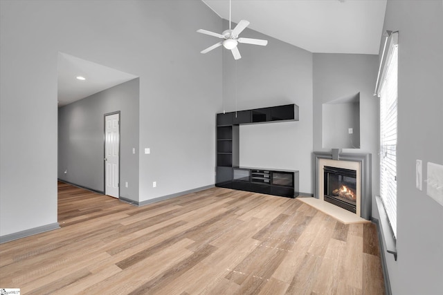 unfurnished living room with high vaulted ceiling, ceiling fan, a glass covered fireplace, and wood finished floors