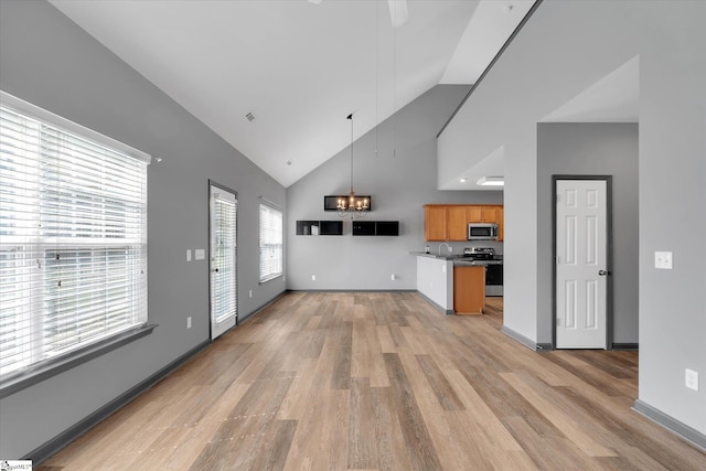 unfurnished living room with an inviting chandelier, visible vents, light wood-style floors, baseboards, and high vaulted ceiling