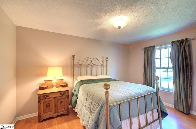 bedroom with baseboards, a textured ceiling, and light wood-style flooring