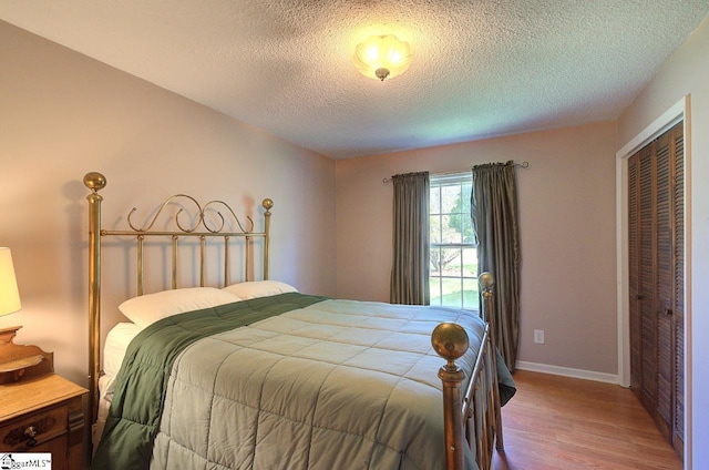 bedroom with baseboards, a textured ceiling, wood finished floors, and a closet