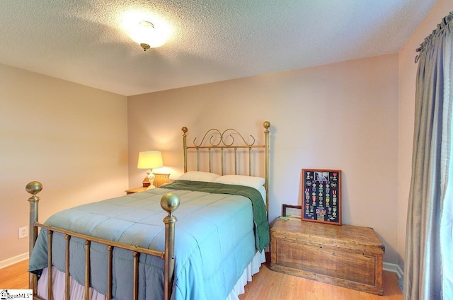 bedroom with a textured ceiling, baseboards, and wood finished floors