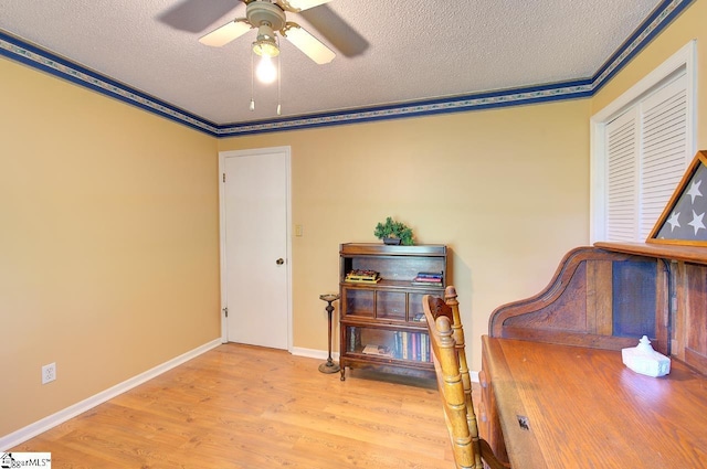 interior space featuring a ceiling fan, a textured ceiling, wood finished floors, baseboards, and ornamental molding