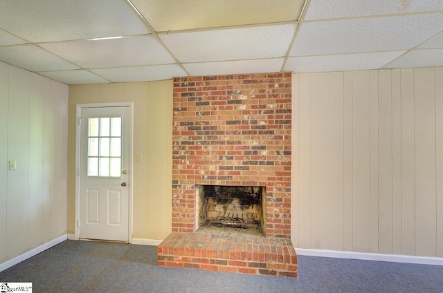 unfurnished living room featuring carpet floors, wooden walls, a paneled ceiling, and a fireplace