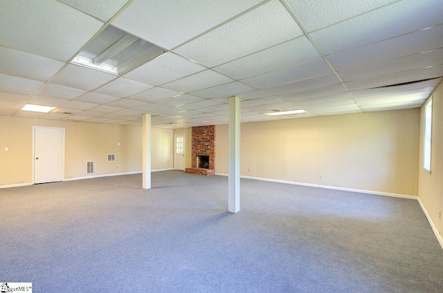 basement featuring carpet floors, a drop ceiling, a brick fireplace, and visible vents