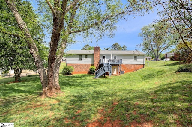 rear view of house featuring stairs, brick siding, a deck, a chimney, and a yard