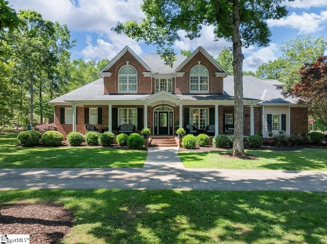 view of front of property featuring covered porch, a front lawn, and brick siding