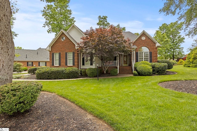 view of front of property with covered porch, brick siding, a front yard, and roof with shingles