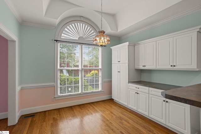 unfurnished dining area with a notable chandelier, baseboards, light wood-type flooring, visible vents, and ornamental molding