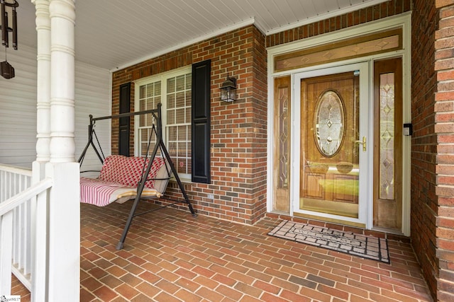entrance to property featuring a porch and brick siding