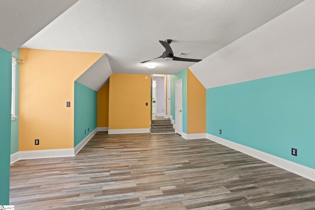 additional living space featuring wood finished floors, baseboards, a textured ceiling, a ceiling fan, and vaulted ceiling