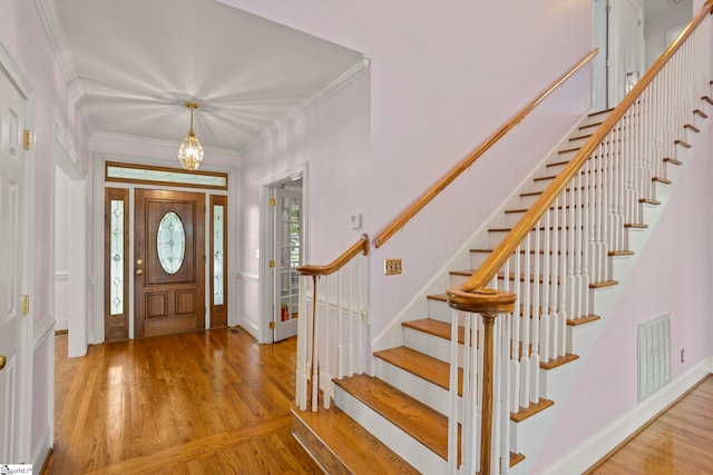 foyer entrance featuring a notable chandelier, stairs, wood finished floors, visible vents, and ornamental molding
