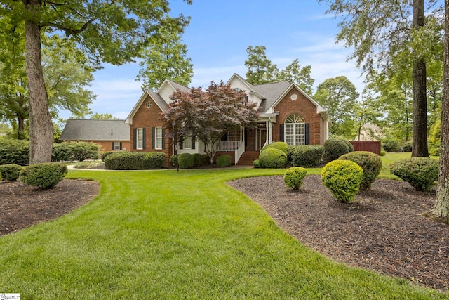 view of front of property with brick siding, a shingled roof, a front yard, and a porch