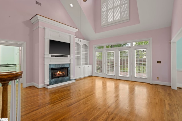 unfurnished living room with light wood finished floors, a fireplace, high vaulted ceiling, baseboards, and visible vents
