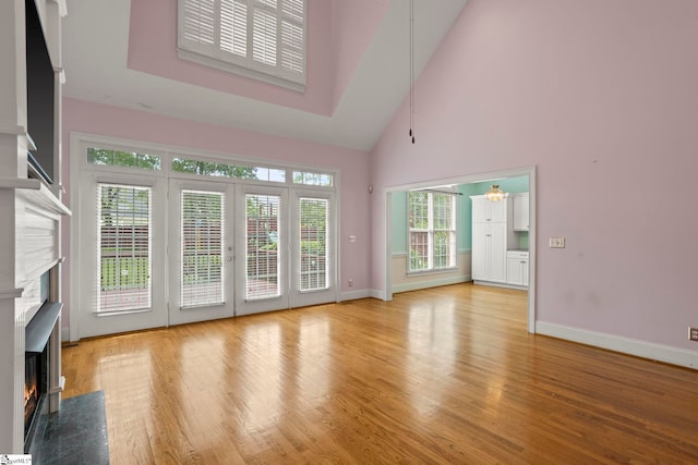 unfurnished living room featuring high vaulted ceiling, baseboards, a fireplace, and light wood-style flooring