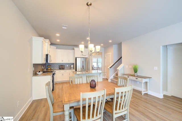 dining space with visible vents, baseboards, light wood finished floors, a notable chandelier, and stairs