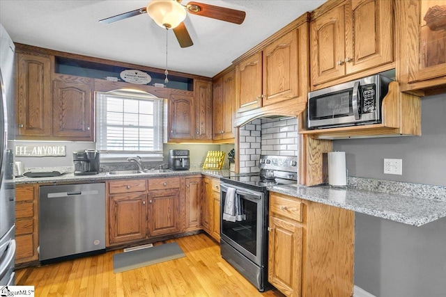 kitchen featuring light stone counters, a sink, light wood-style floors, stainless steel appliances, and a ceiling fan