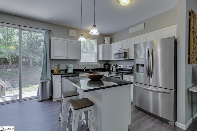 kitchen featuring white cabinets, dark wood-style flooring, dark countertops, stainless steel appliances, and pendant lighting