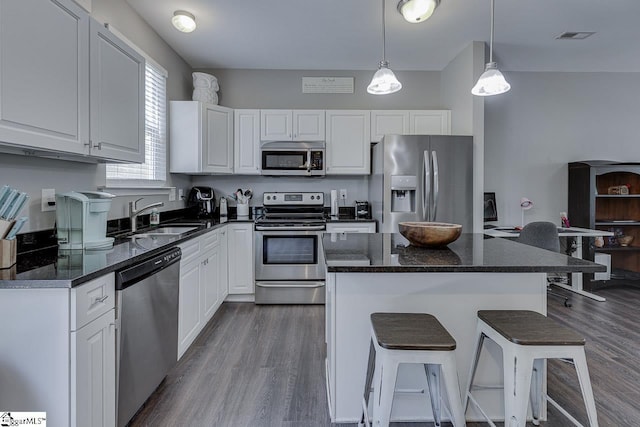 kitchen with appliances with stainless steel finishes, a sink, a kitchen breakfast bar, dark wood finished floors, and white cabinetry