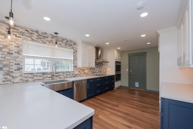kitchen with a sink, appliances with stainless steel finishes, blue cabinets, and wall chimney exhaust hood