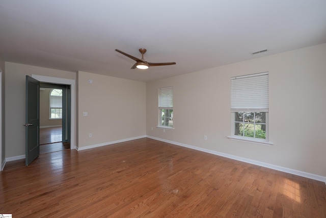 unfurnished room with plenty of natural light, a ceiling fan, baseboards, and wood finished floors