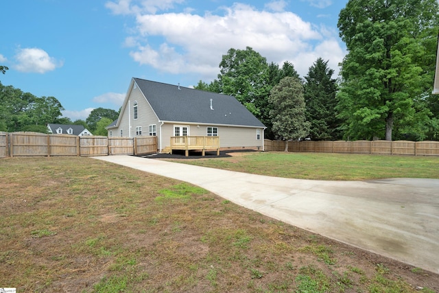 rear view of property featuring a fenced backyard, a wooden deck, a yard, and driveway