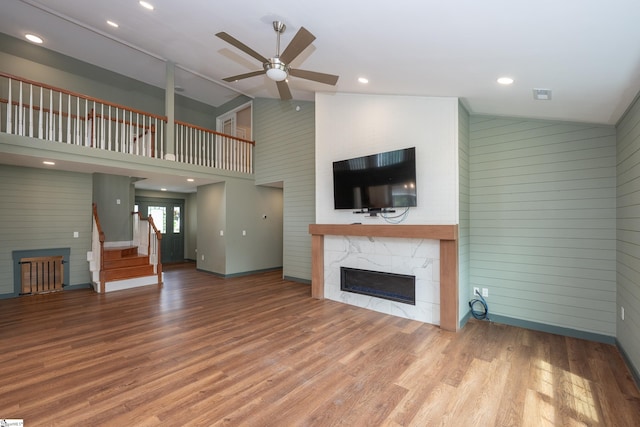 unfurnished living room with a tiled fireplace, wood walls, ceiling fan, and wood finished floors