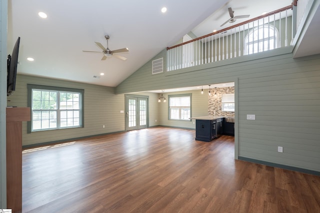 unfurnished living room with high vaulted ceiling, wood walls, a ceiling fan, baseboards, and dark wood-type flooring