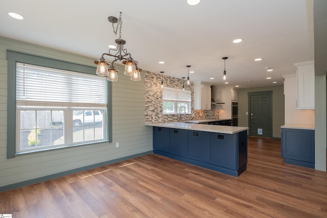 kitchen with light countertops, dark wood finished floors, wall chimney exhaust hood, a peninsula, and white cabinetry