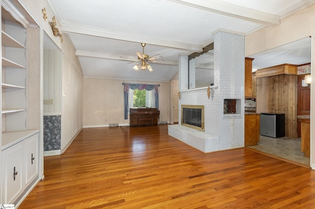 unfurnished living room with a ceiling fan, visible vents, a brick fireplace, lofted ceiling with beams, and light wood finished floors