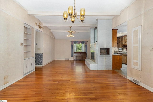 unfurnished living room with a brick fireplace, a chandelier, built in shelves, and light wood finished floors