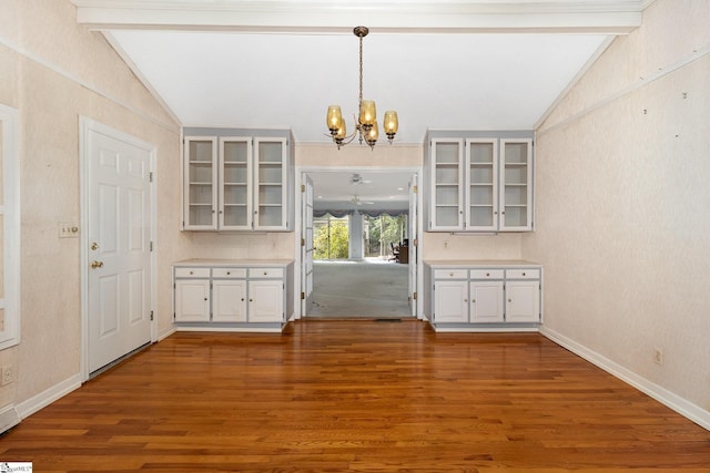 unfurnished dining area featuring vaulted ceiling with beams, baseboards, wood finished floors, and an inviting chandelier