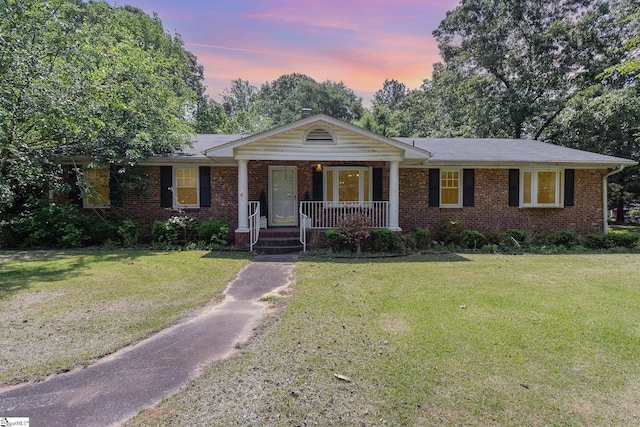 ranch-style home featuring covered porch, brick siding, and a front yard