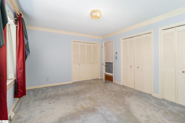 unfurnished bedroom with two closets, baseboards, ornamental molding, and carpet floors