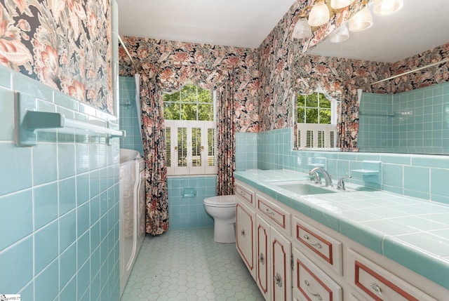 full bathroom featuring a healthy amount of sunlight, tile walls, vanity, and toilet