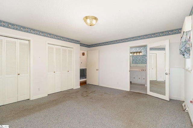 unfurnished bedroom featuring ensuite bathroom, multiple closets, baseboards, and carpet