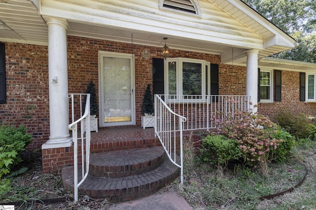 view of exterior entry featuring a porch and brick siding