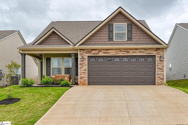craftsman inspired home featuring a shingled roof, stone siding, a front yard, covered porch, and driveway
