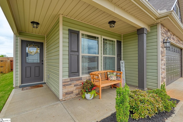 doorway to property with a porch, driveway, a garage, fence, and stone siding