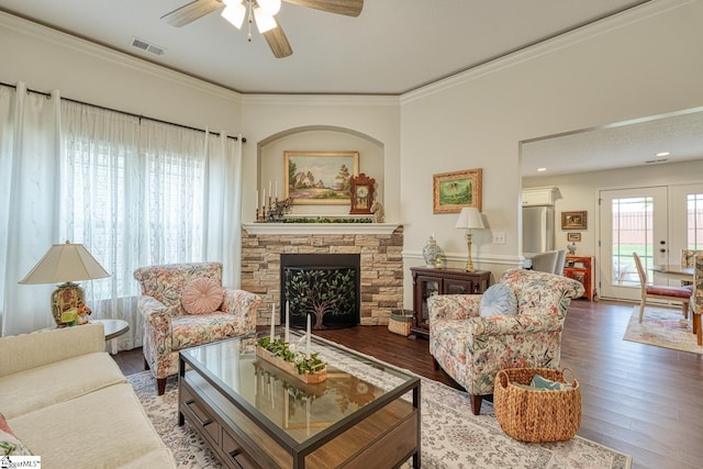 living area featuring a ceiling fan, visible vents, a fireplace, wood finished floors, and ornamental molding