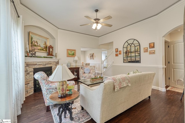 living area featuring crown molding, a stone fireplace, dark wood-style floors, stairway, and a ceiling fan