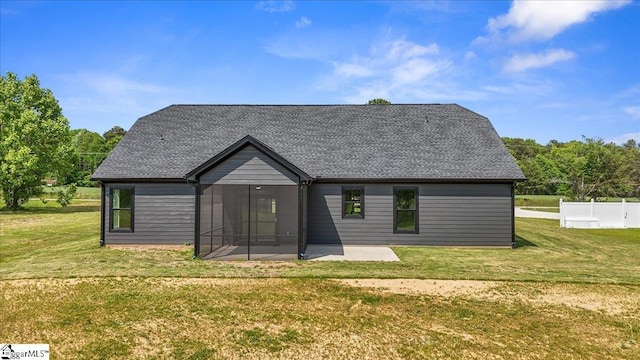 rear view of property featuring a lawn, a patio, a sunroom, and roof with shingles
