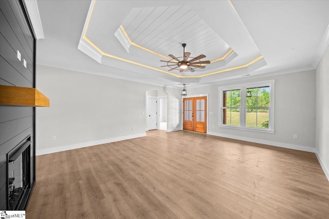 unfurnished living room with baseboards, wood finished floors, a tray ceiling, and a large fireplace