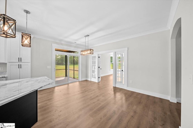 unfurnished dining area featuring crown molding, arched walkways, wood finished floors, and a wealth of natural light